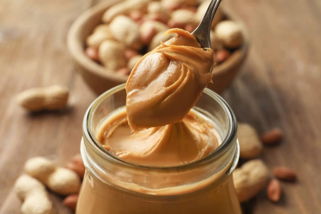 Spoon and glass jar with creamy peanut butter.