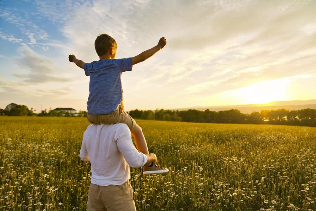 Child on the shoulder of his father during sunset.