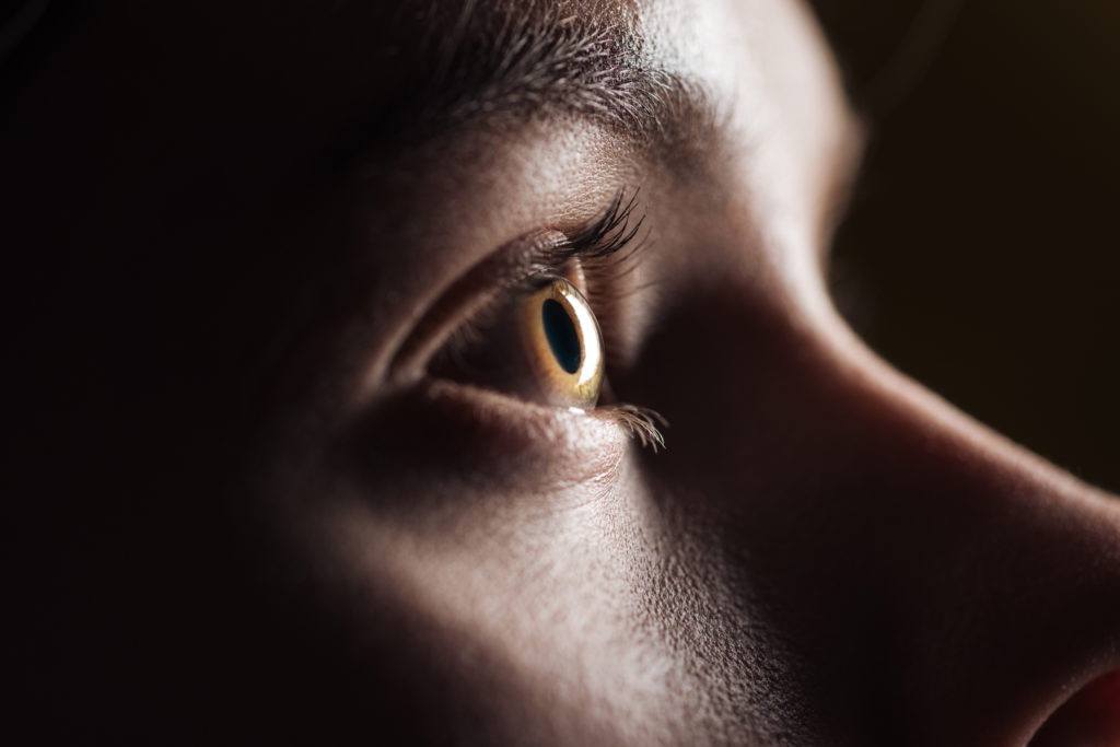 Close-up view of young woman's eye looking away in the darkness.