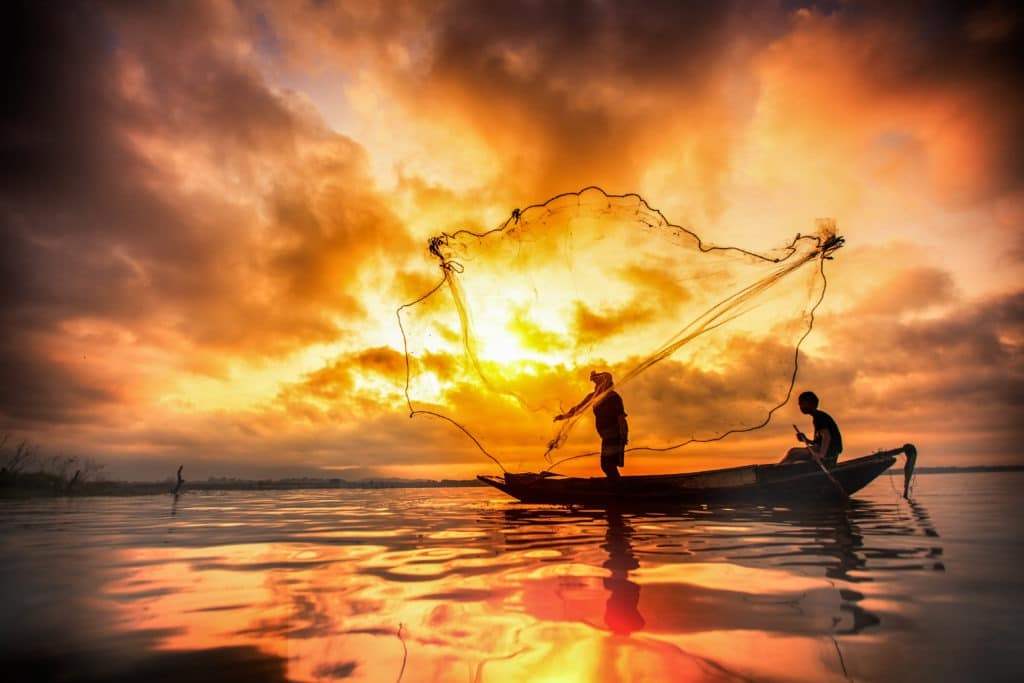 Fishermen in a lake with net, fishing during sunset.
