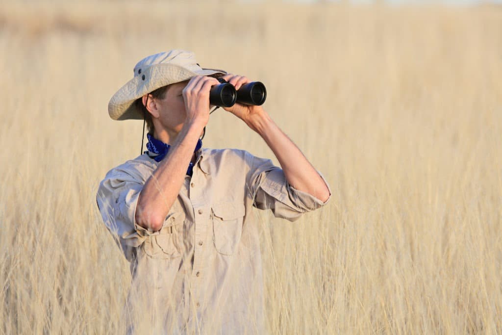 Man in the safari looking through binoculars.